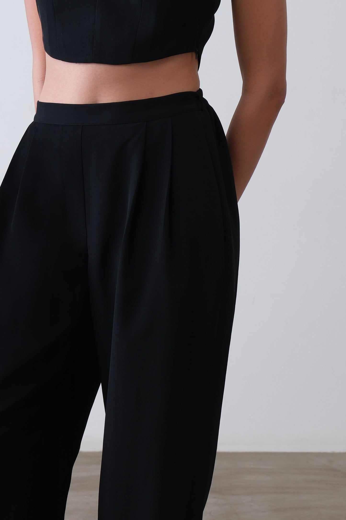 Close up of satin ankle cuff and pleat detail on black viscose blend trousers
