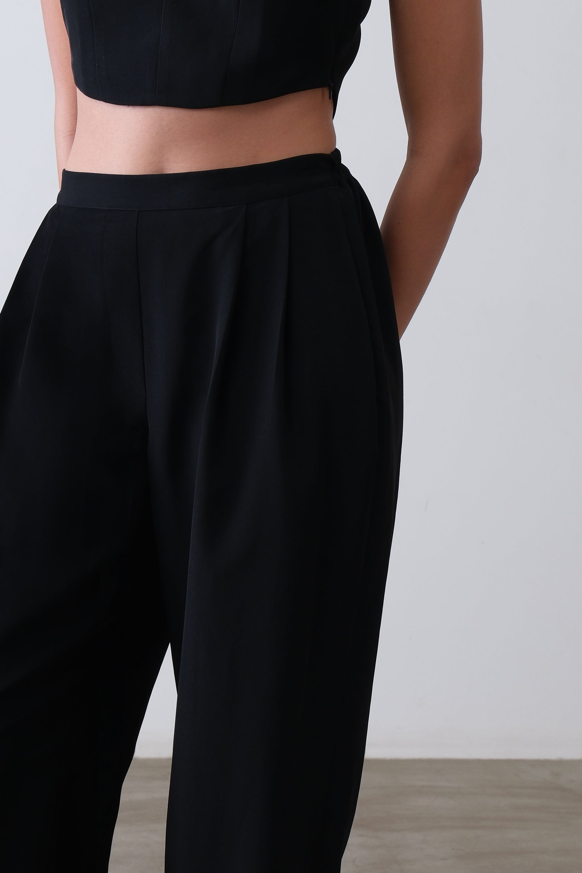 Close up of satin ankle cuff and pleat detail on black viscose blend trousers