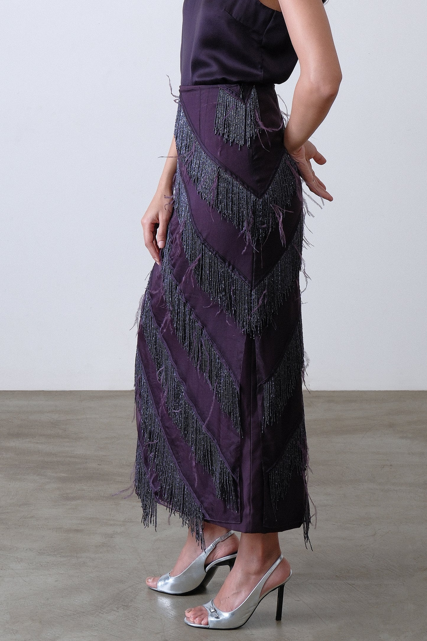 Side view of deep plum layered skirt with beaded fringe and feather accents